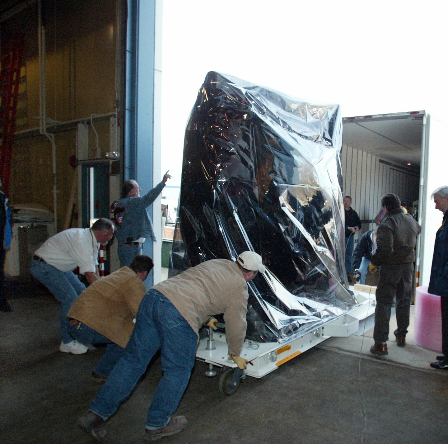 Wrapped in protective film, the MESSENGER spacecraft is loaded into a moving van