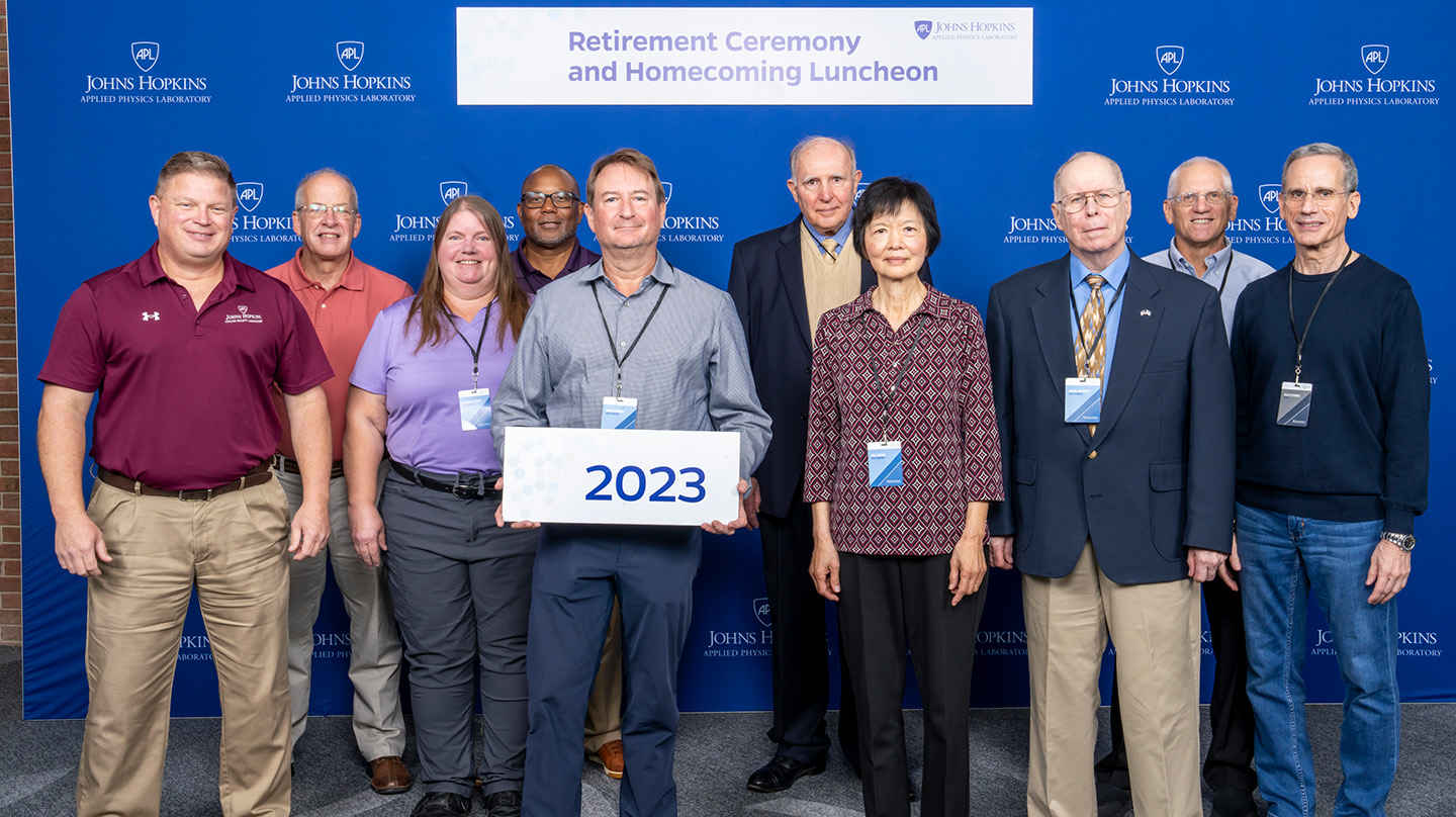 Attendees at APL's 2023 Retirement Ceremony and Homecoming Luncheon pose for a photo with Ralph Semmel and Erik Johnson.