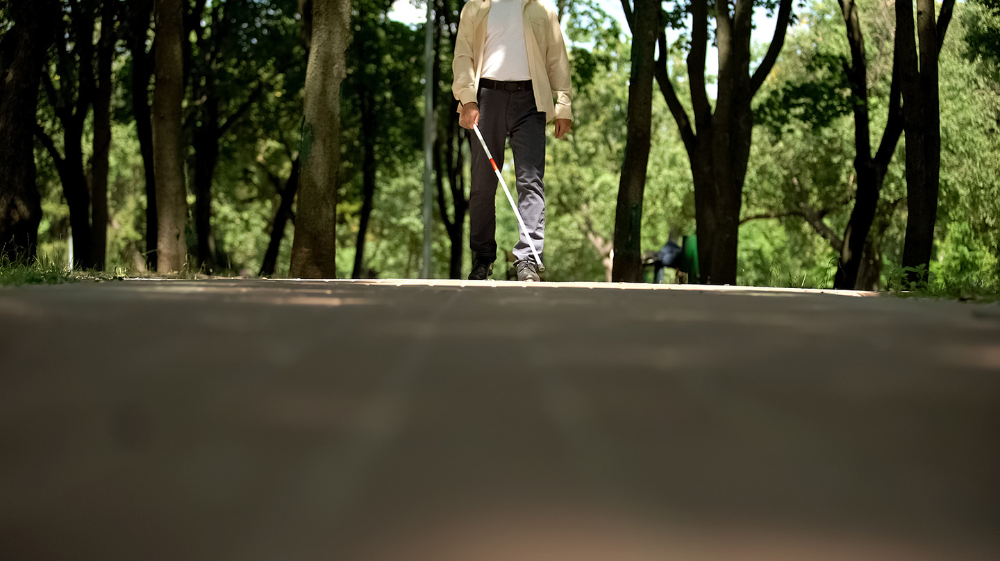 Blind person walking in a park, using a cane to locate and navigate around obstructions. (Credit: Bigstock)