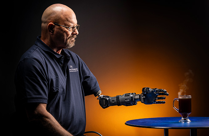 A person uses the modular prosthetic limb to reach for a hot drink